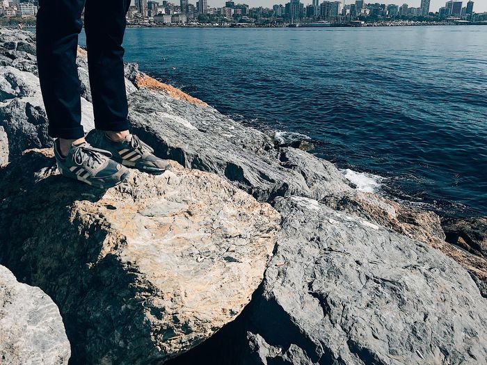 Low section of man standing on rock by sea