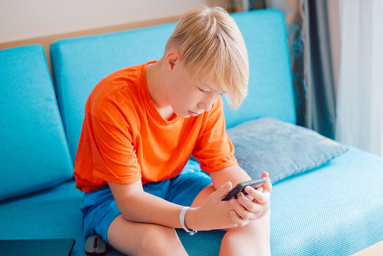 Side view of boy using mobile phone while lying on bed at home