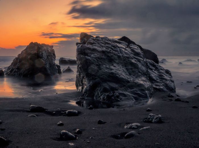 Rocks on beach against cloudy sky during sunset