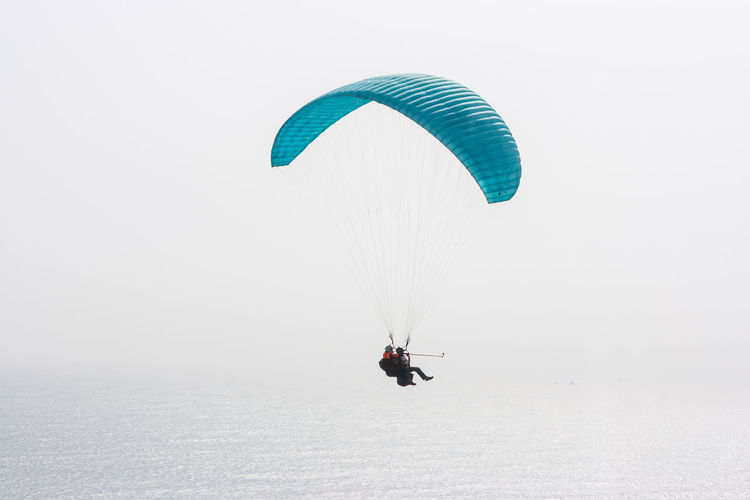 High angle view of people paragliding over ocean against clear sky