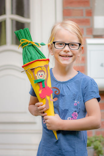 Portrait of smiling girl holding toy while standing against house