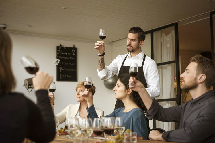 Man standing by people and analyzing wineglass at table