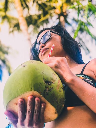 Low angle view of young woman holding coconut