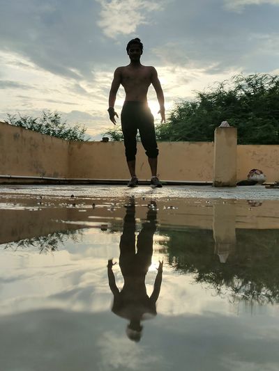 Full length of shirtless man standing in lake against sky