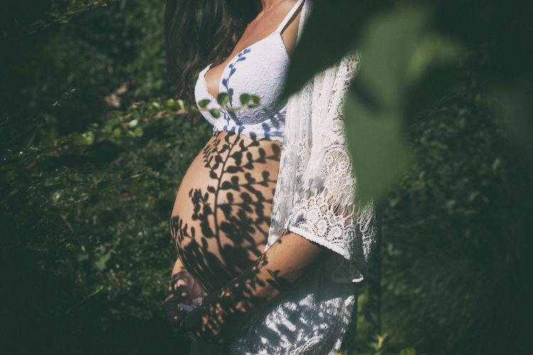 Midsection of pregnant woman standing amidst plants during sunny day