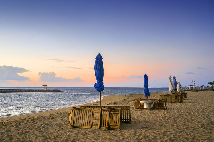 Deck chairs on beach against sky during sunset