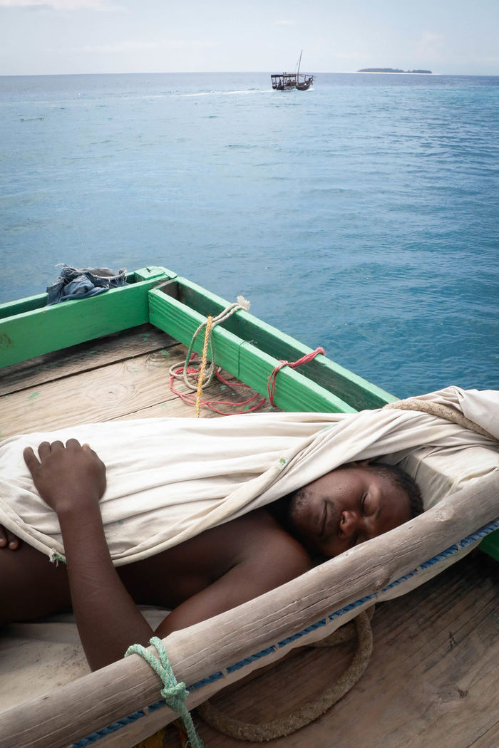 Naked man with blanket sleeping on pier in sea