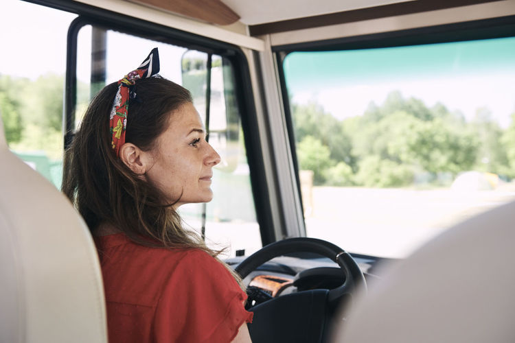Thoughtful mature woman sitting on driver's seat in camper trailer during summer