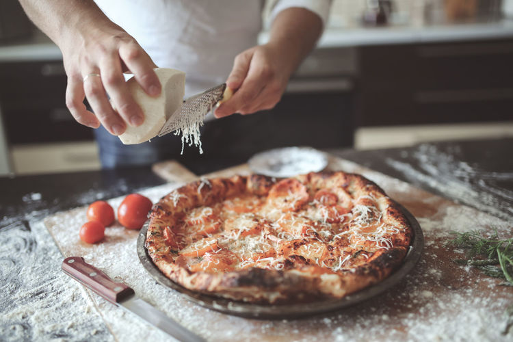 Male hands rubbed cheese grated on pizza, pizza cooking in a real home interior lifestyle