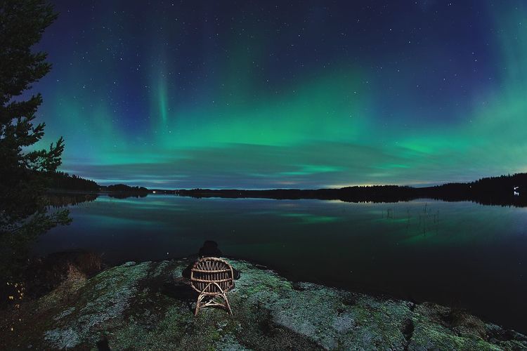 Rear view of person sitting on chair by lake against aurora polaris in sky