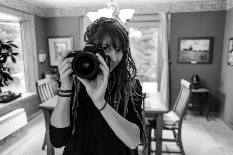 Portrait of young woman holding camera at home