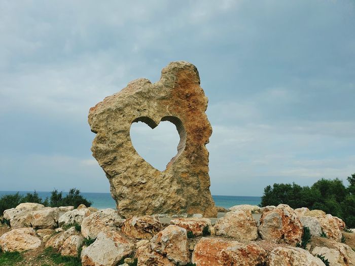 Low angle view of heart shape on rock against sky