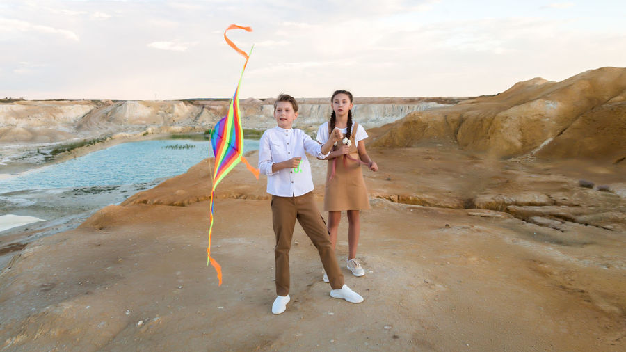 A girl watches as boy deftly launches a kite into the sky.