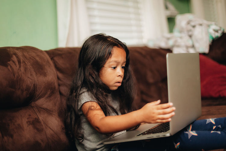 Mixed race young girl at home on the sofa using a laptop computer for learning 