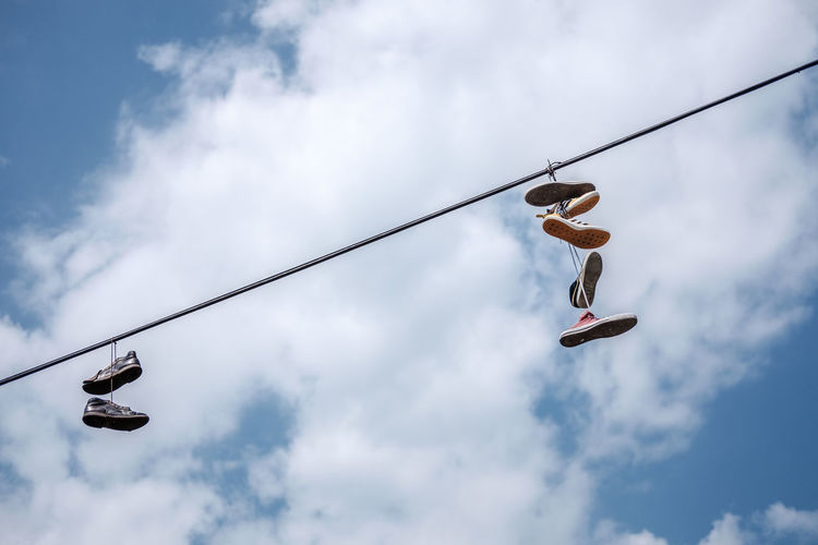 Low angle view of shoes hanging on cable against sky