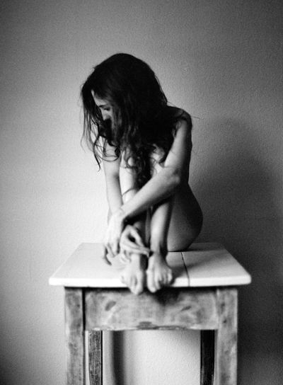 Full length of naked woman sitting on stool against wall at home