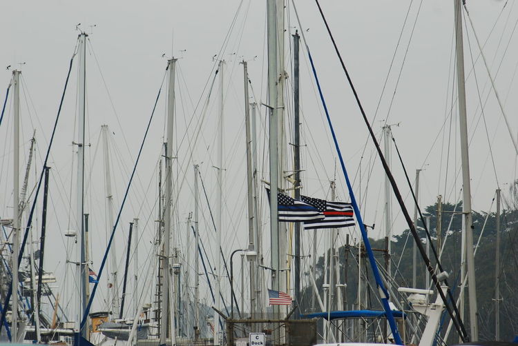 Sailboats moored in harbor against sky with thin blue line flag