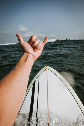 Cropped image of hand gesturing against in sea against sky