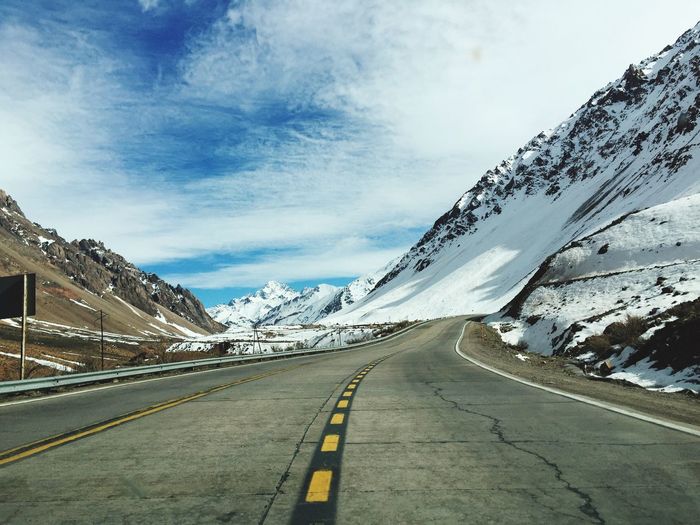 Surface level shot of road amidst snowcapped mountains against sky