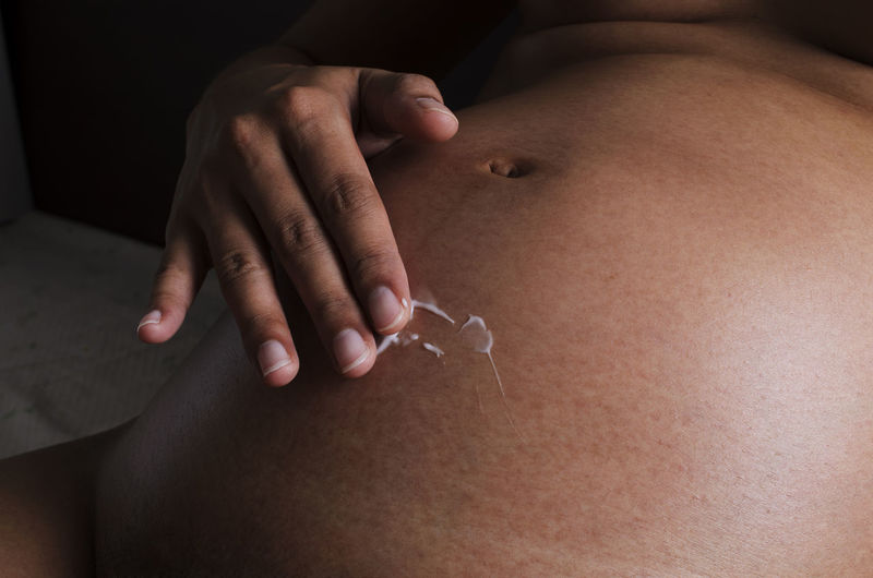 Midsection of pregnant woman applying moisturizer on her belly