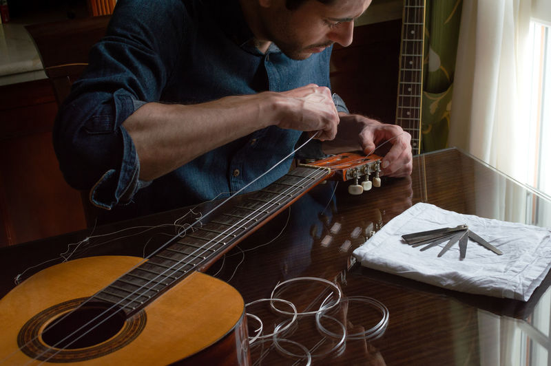 Man adjusting strings in guitar on table at home