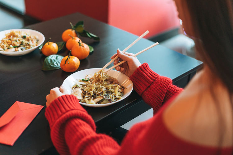Asian woman in red clothes eating noodles with bamboo chopsticks in chinese vietnamese restaurant