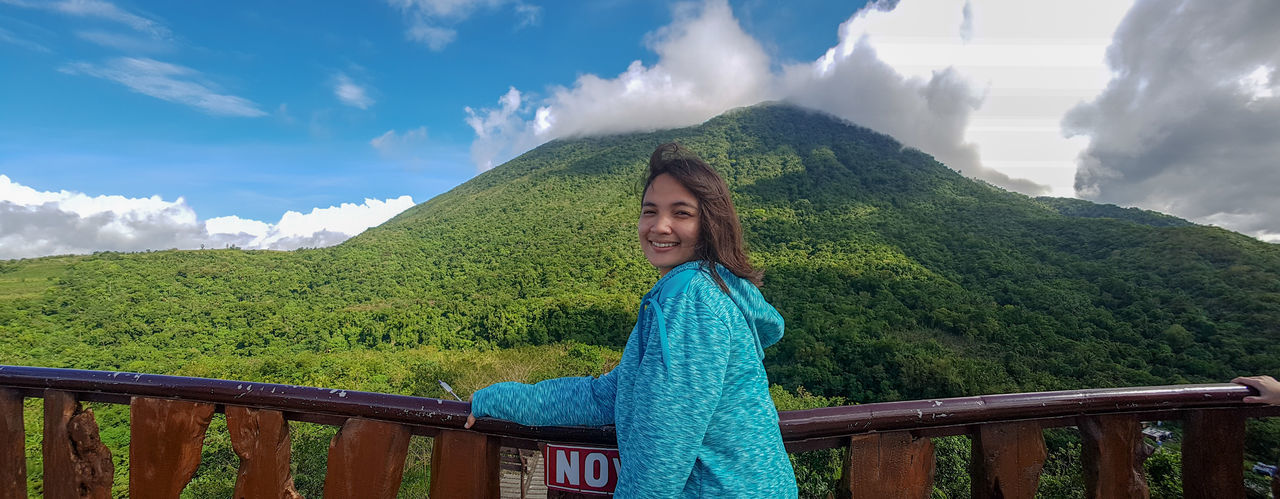 Side view portrait of woman smiling while standing against mountains