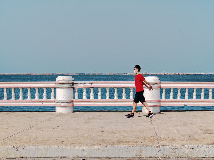 Kid wearing medical mask having fun walking along footpath by the sea