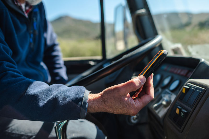 Side view of elderly male traveler in casual clothes using gps navigator on smartphone while sitting in car during road trip in countryside