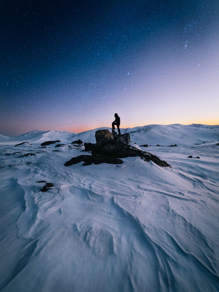 Silhouette man standing on rock at snow covered mountains against sky