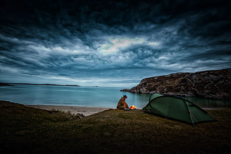 Man sitting by tent against sea and sky