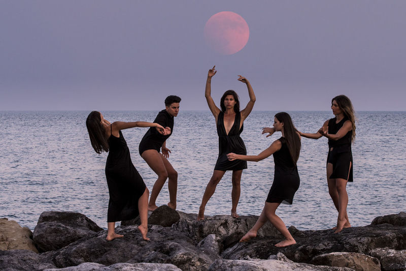 Fashion models posing on rocks by sea against sky