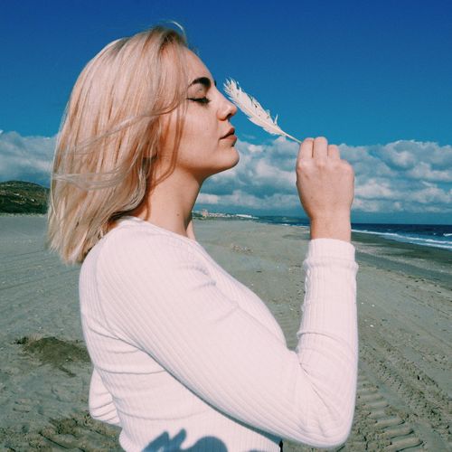 Side view of young woman with feather standing at beach