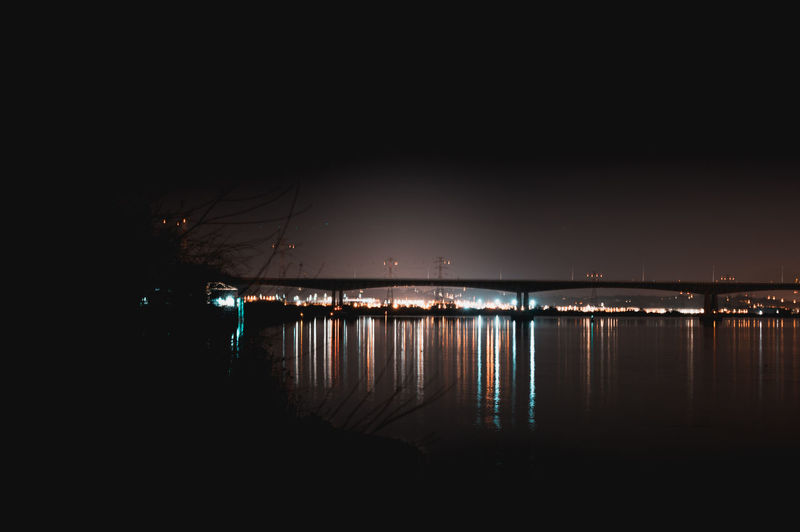 Silhouette bridge over sea against sky at night