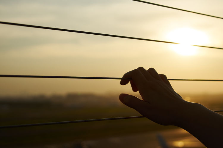Close-up of silhouette hand holding sun against sky during sunset