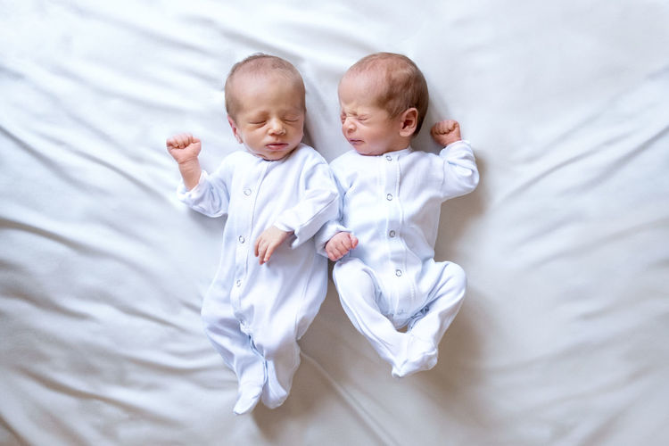 Newborn twins on the bed, in the arms of their parents, on a white background. life style, emotions
