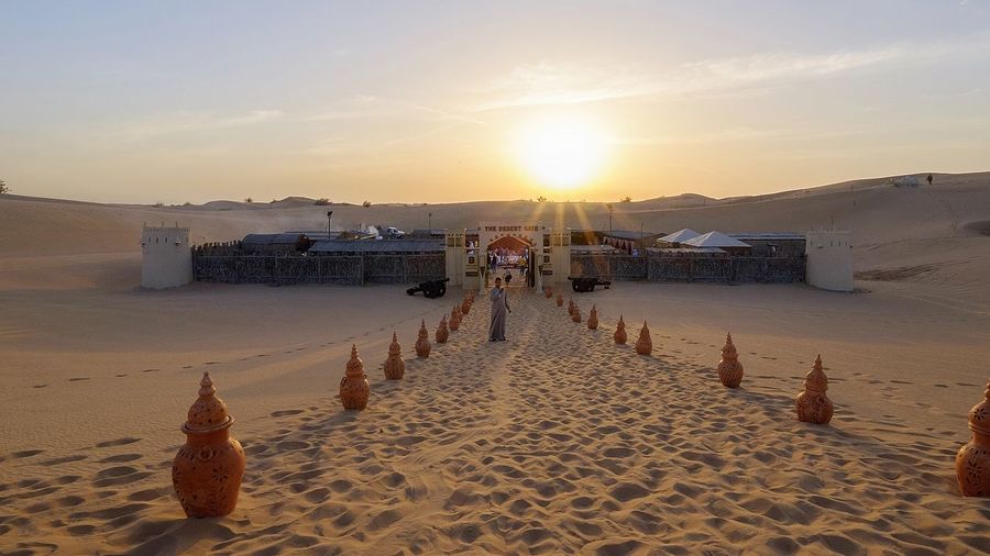 Person standing on pathway amidst decorative urns at desert during sunrise