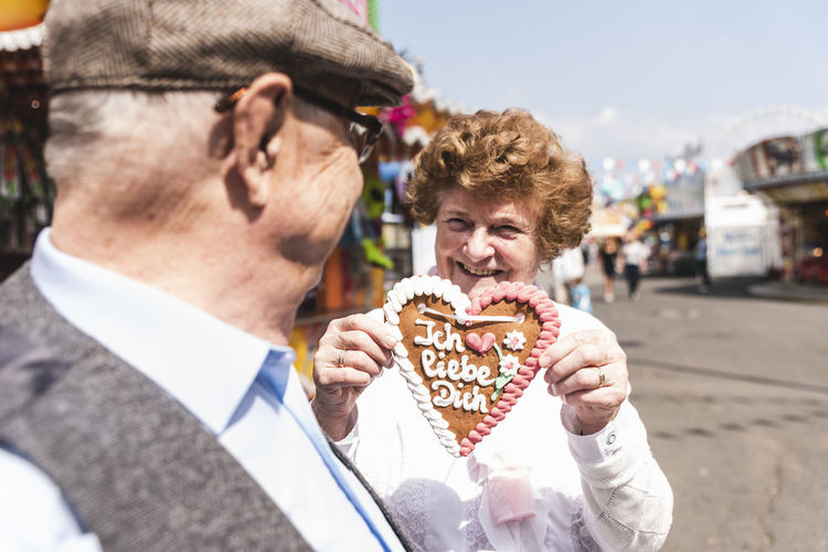 Portrait of hasmiling senior woman presenting gingerbread heart on fair