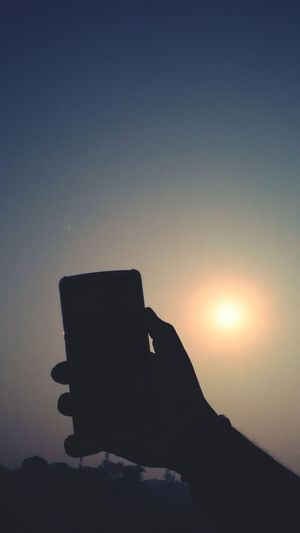 Close-up of silhouette person holding camera against sky during sunset