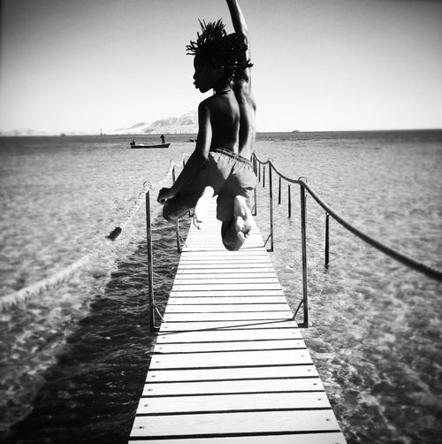 Woman jumping on pier at sea