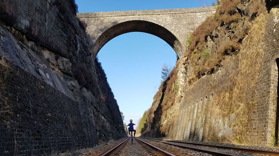 Rear view of boy riding bicycle on railroad track between walls
