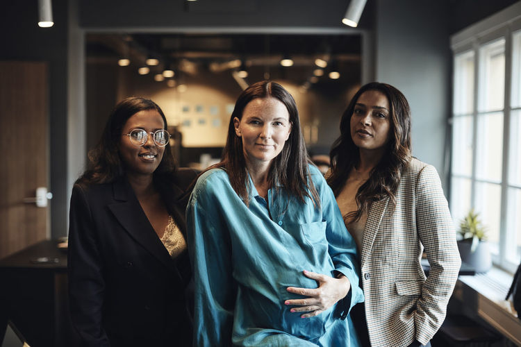 Confident businesswomen with pregnant female colleague at office