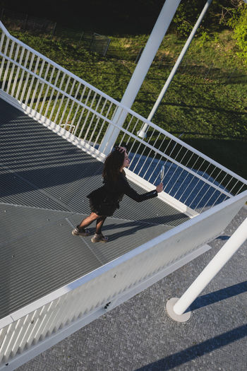 High angle view of young woman holding hand mirror while standing on elevated walkway
