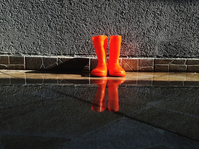 Orange rubber boots on puddle against wall