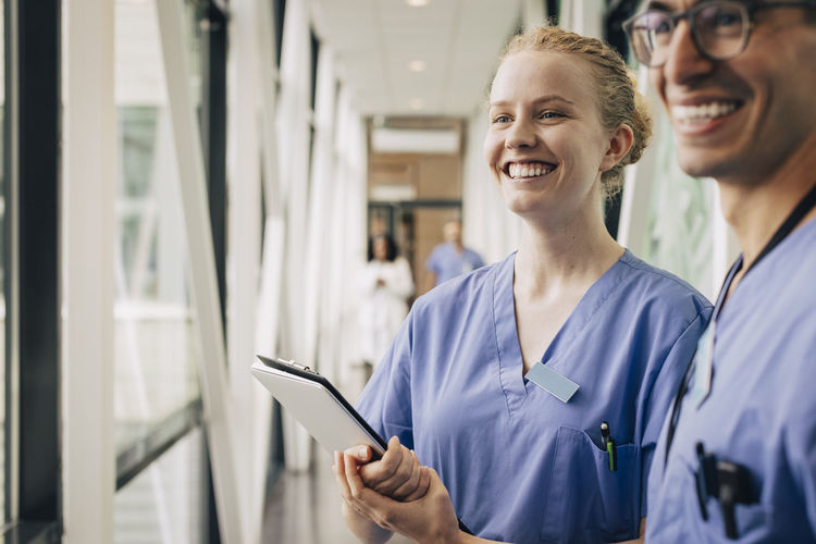 Happy female nurse looking away while holding clipboard at hospital