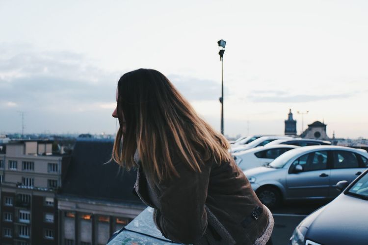 Side view of woman leaning on railing against sky