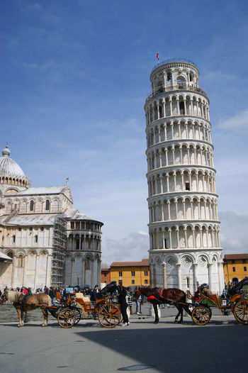 Horse carts by leaning tower of pisa on street in city