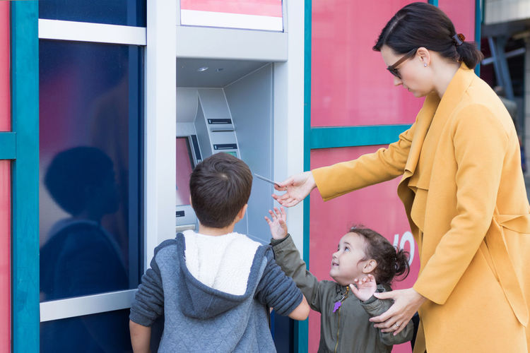 Woman using atm while standing with children in city