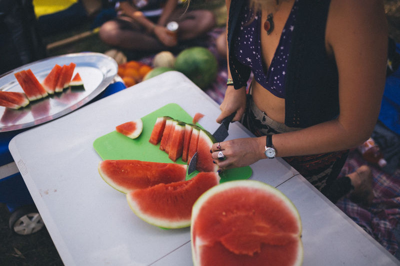 Midsection of woman cutting watermelon at table