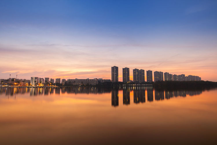 Scenic view of river by buildings against sky during sunset